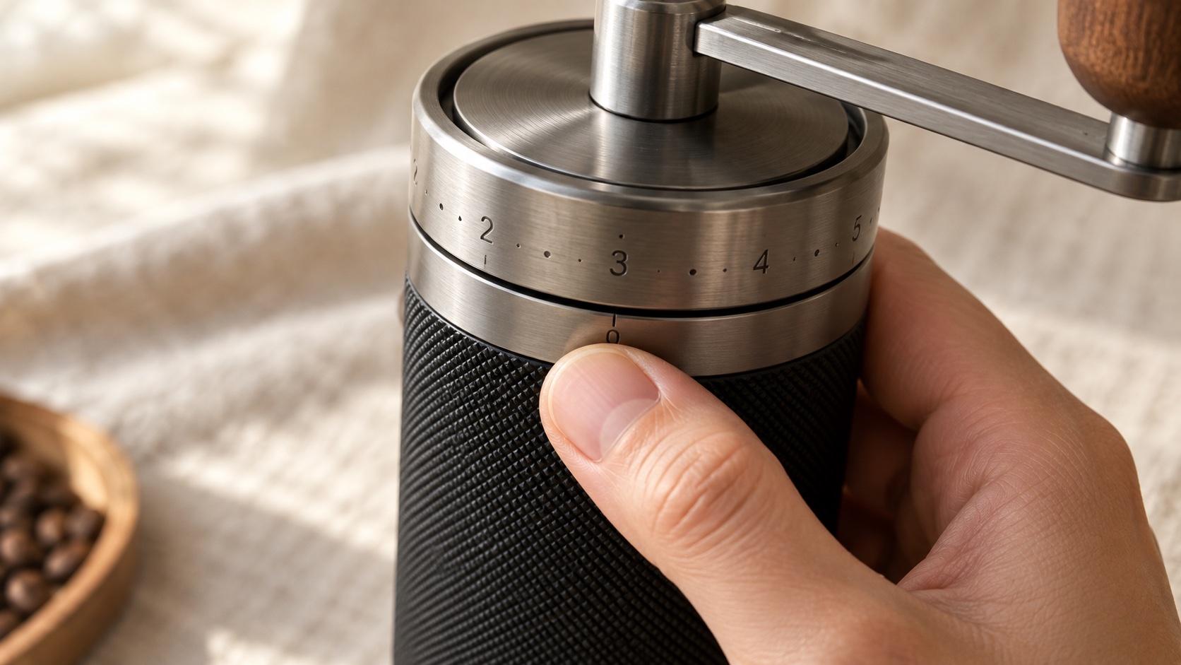 Close view of the numbered adjustment ring at the top of a hand coffee grinder, with a thumb resting beside the zero mark